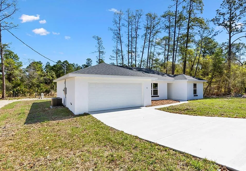 Single-story white house with a two-car garage and a long concrete driveway under a blue sky.