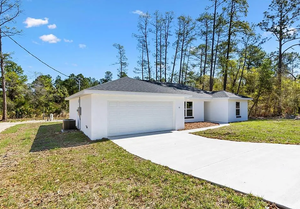 Single-story white house with two-car garage and long driveway under a clear blue sky