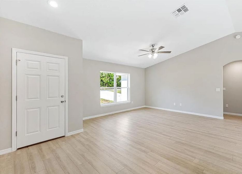 Empty modern room with light wood floors, white walls, ceiling fan, and a window