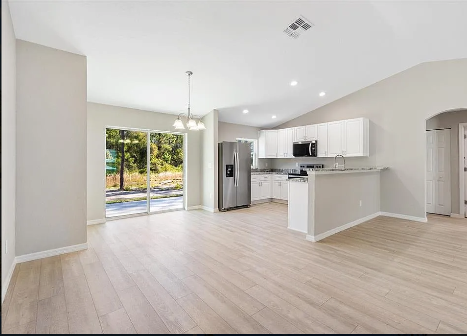 Bright open-plan kitchen and living room with light wood floors, white cabinets, and sliding glass doors to a patio.