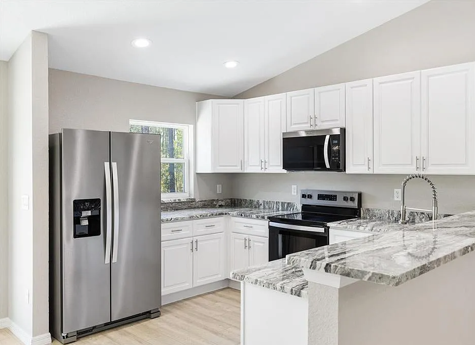 Bright modern kitchen with white cabinets, stainless steel appliances, and marble-pattern countertops
