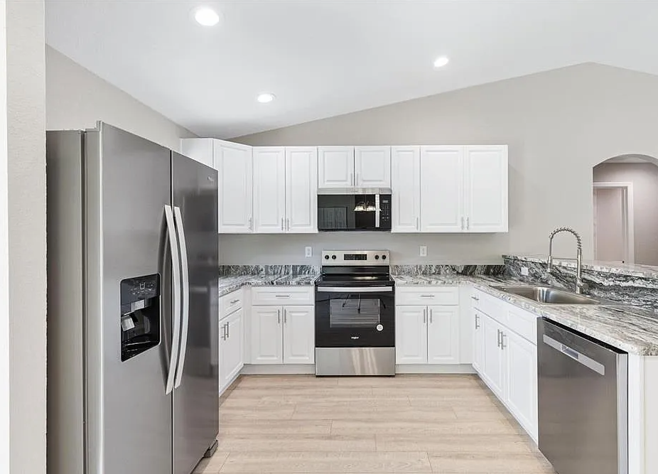 Modern white kitchen with stainless steel appliances, granite countertops, and light wood flooring
