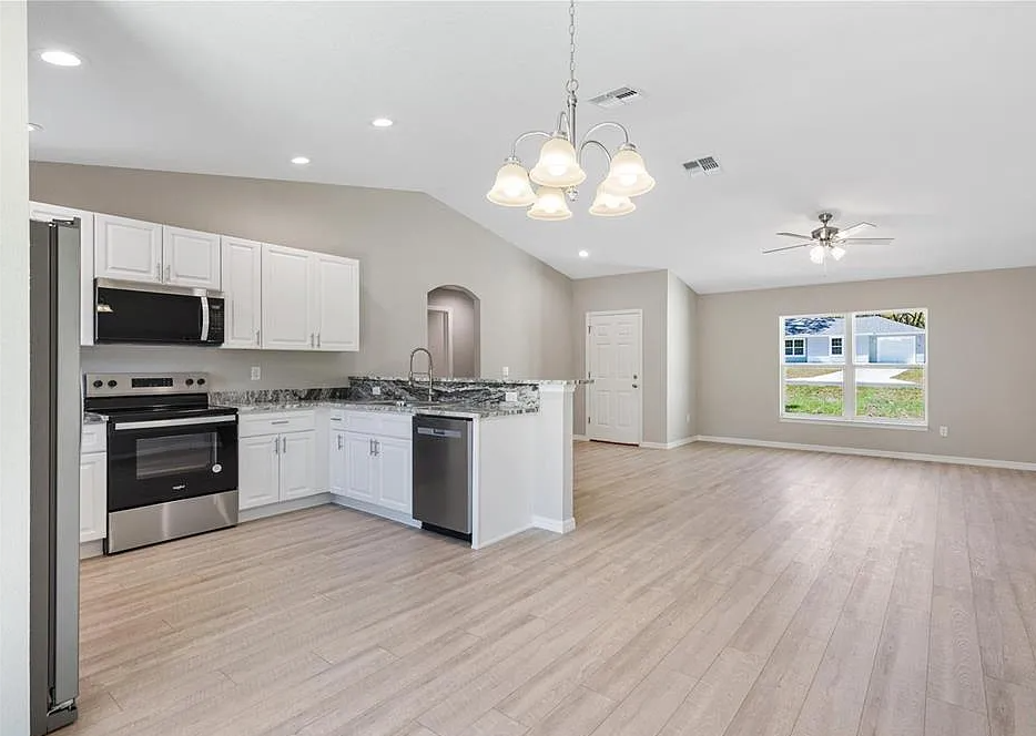 Bright open kitchen and living area with white cabinets, stainless appliances, and light wood floors
