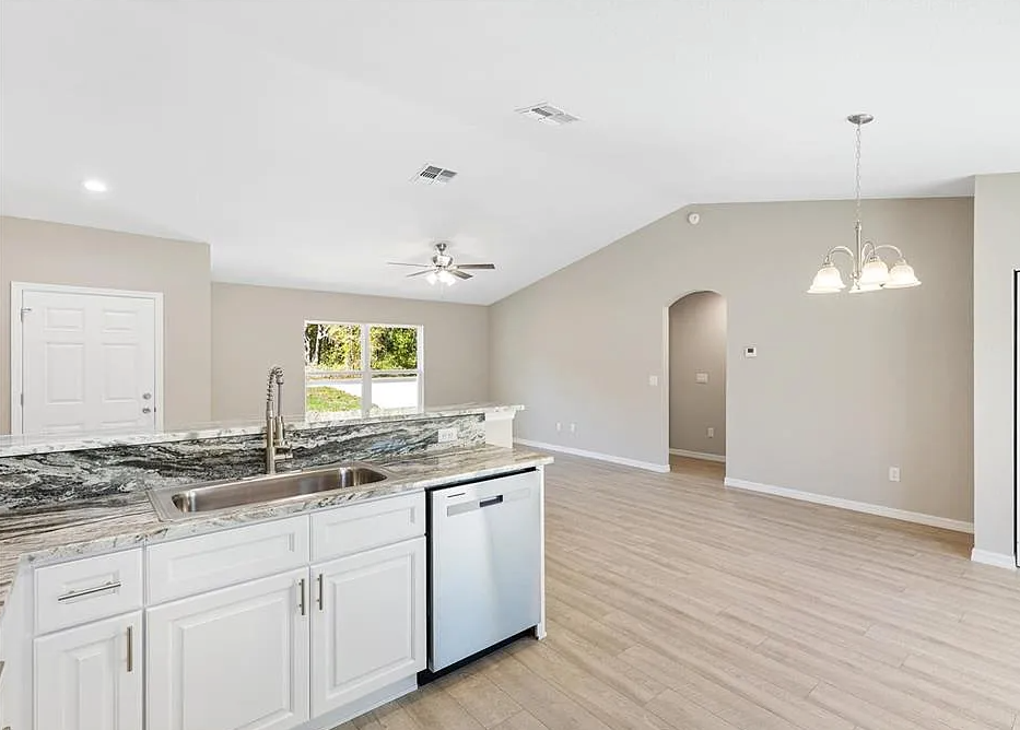 Bright open kitchen and dining area with white cabinets, granite island, and light wood flooring