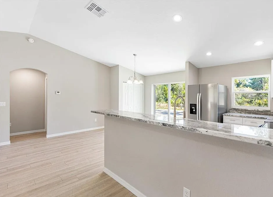 Bright, empty kitchen with granite island, stainless steel fridge, and sliding glass doors to a patio.