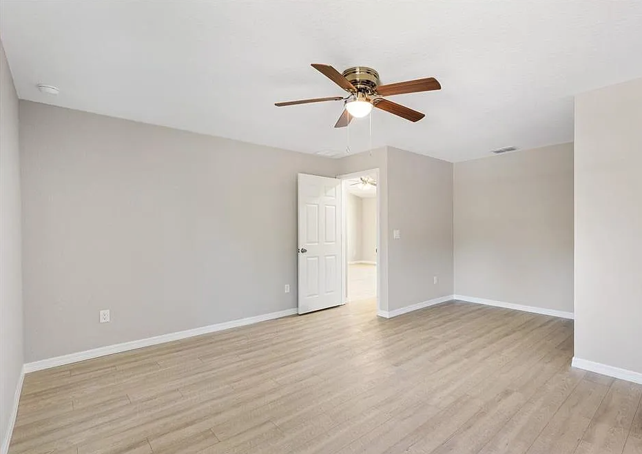 Empty beige bedroom with wood-look flooring, ceiling fan, and open doorway