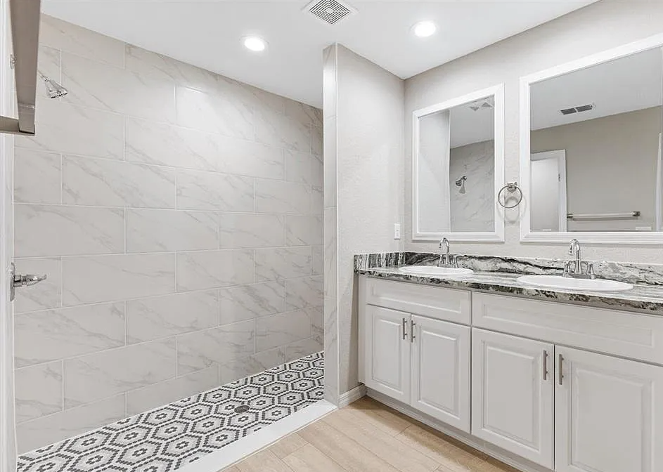 Modern bathroom with white tile shower, patterned floor, and double vanity with mirrors