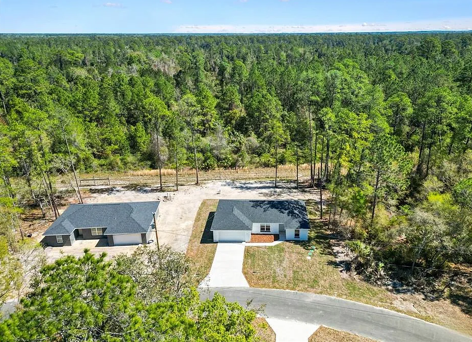 Aerial view of two houses with driveways surrounded by dense green forest.