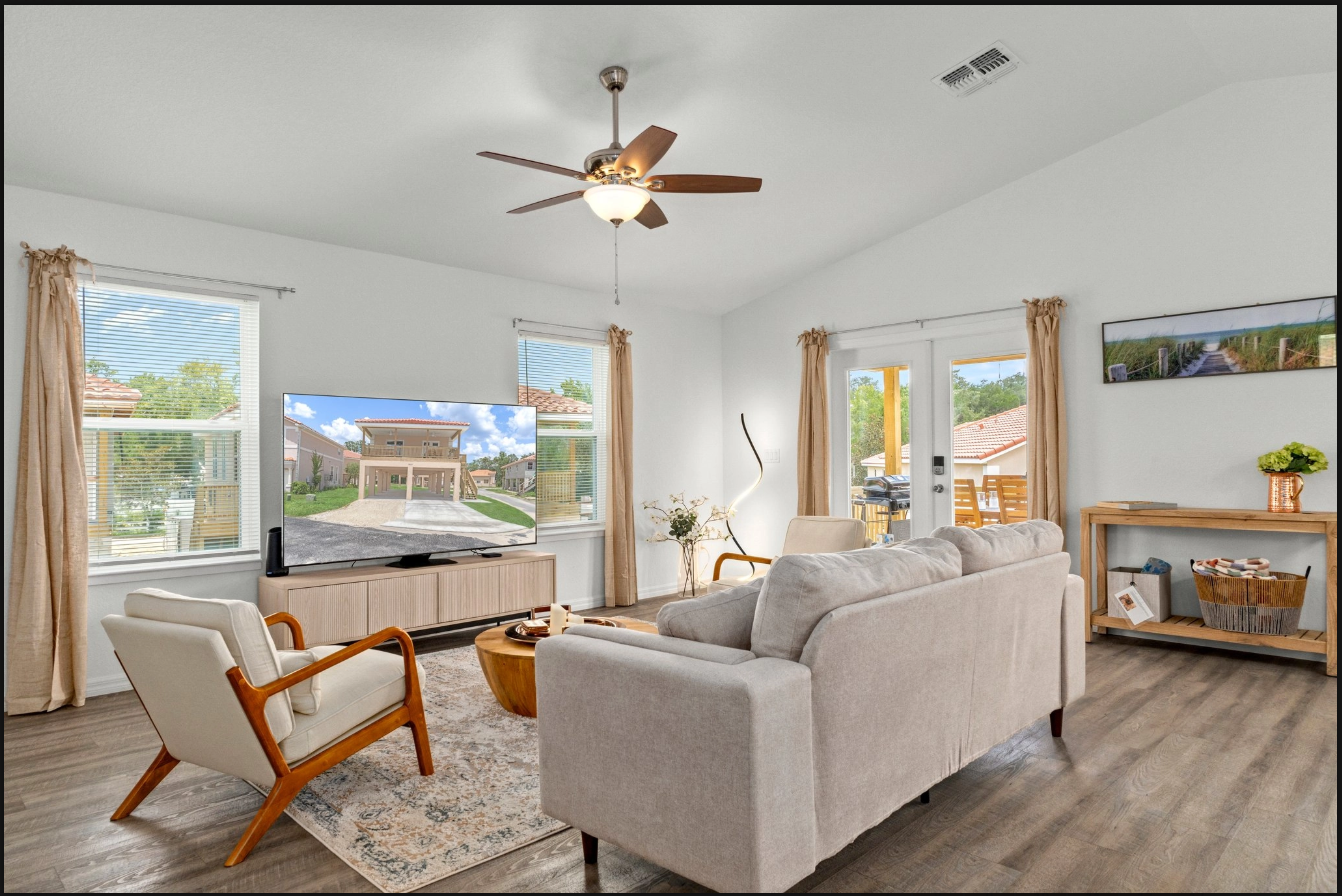 Bright living room with beige sofa, armchair, rug, ceiling fan, and large windows with ocean view