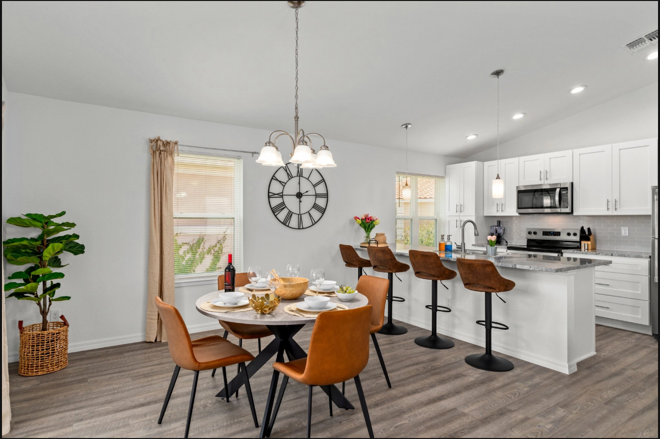 Modern kitchen and dining area with white cabinets, island stools, wooden table, and large wall clock