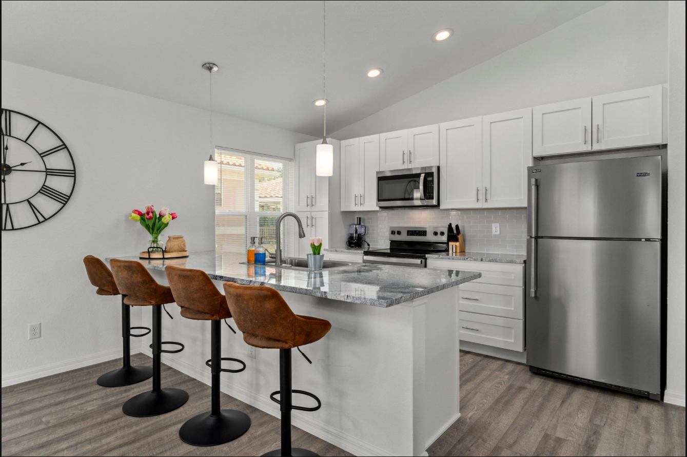 Modern white kitchen with island, stainless steel appliances, and four brown barstools