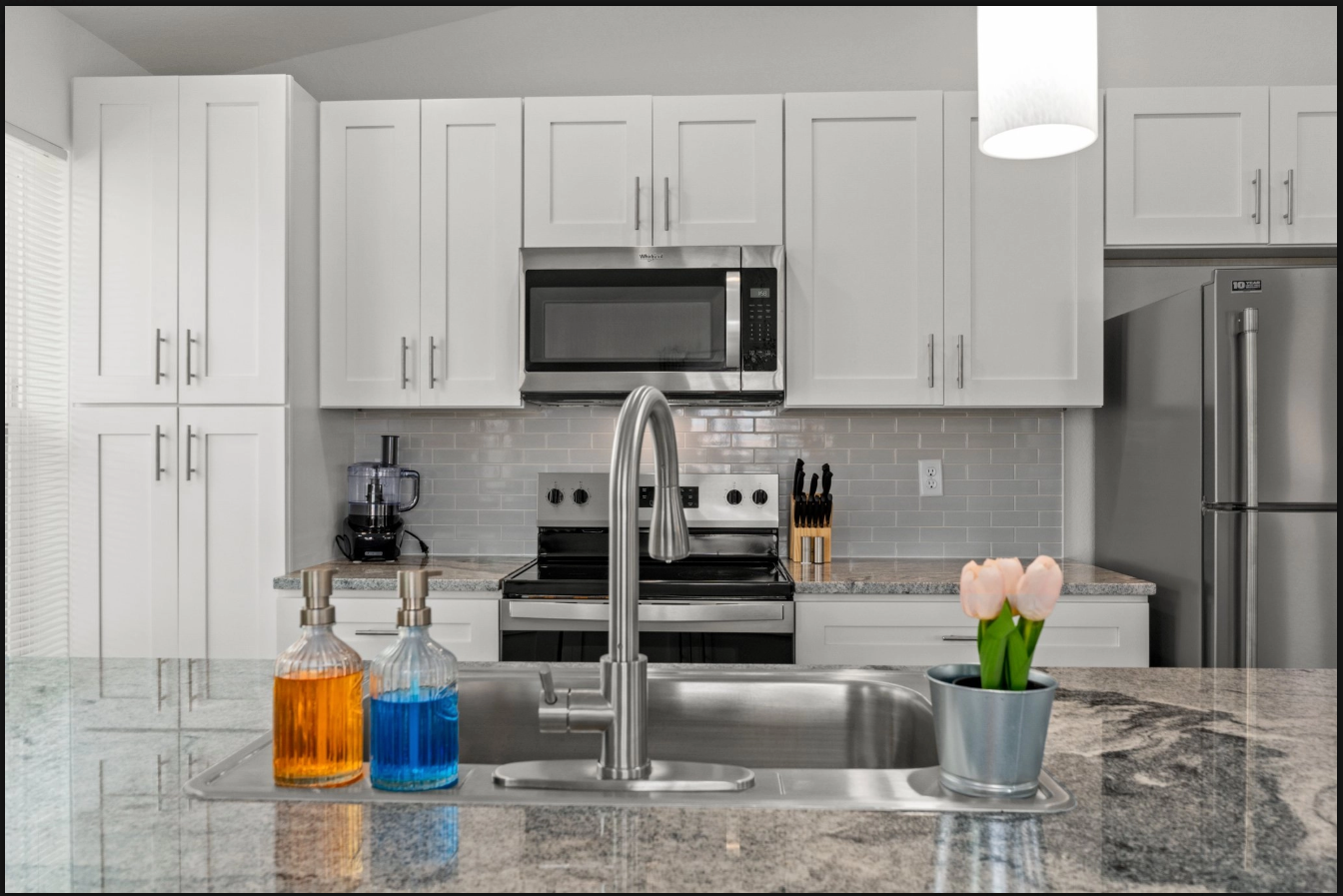 Modern kitchen with white cabinets, stainless appliances, granite island, and small decor items on the counter