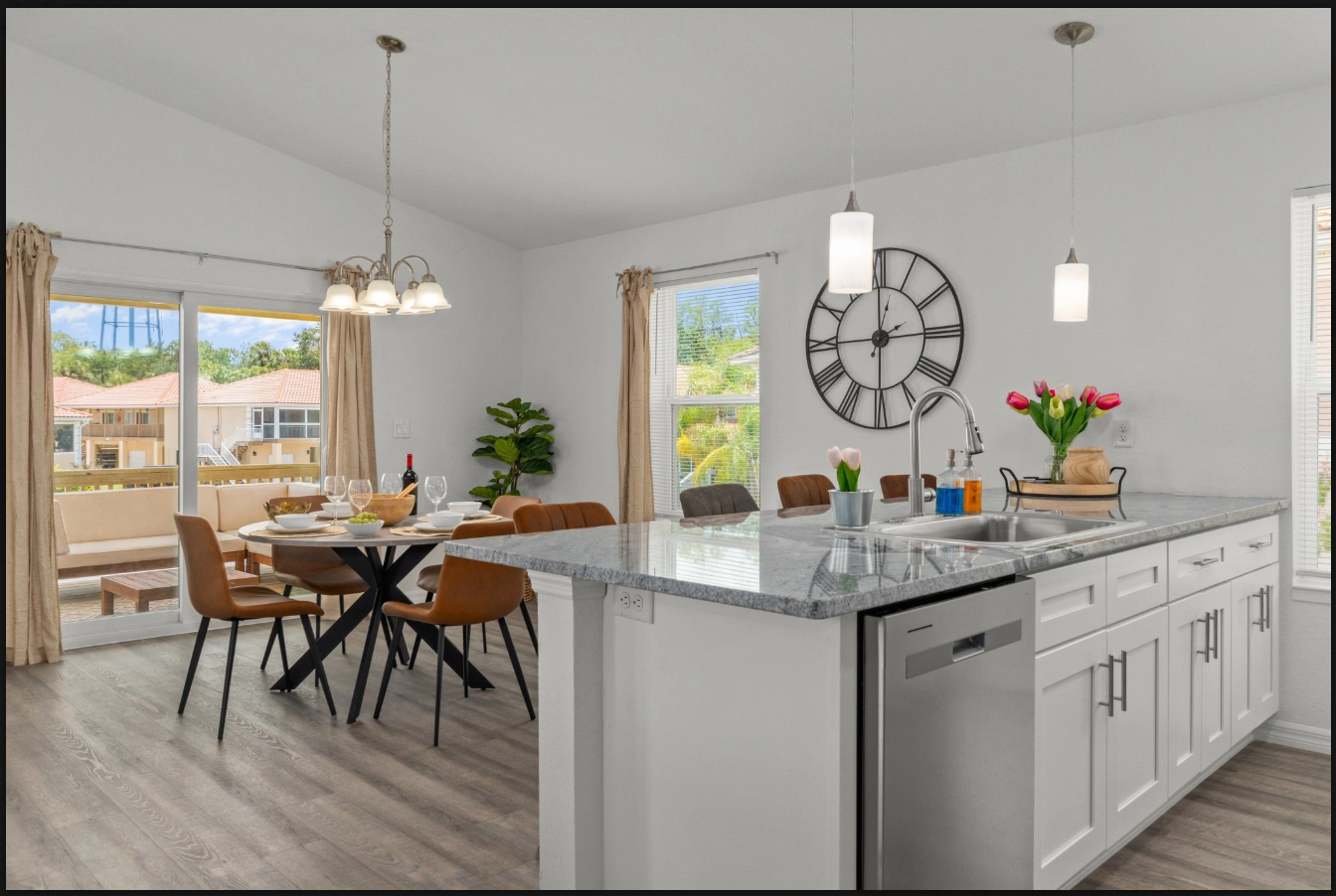 Bright open kitchen with gray island, pendant lights, dining table, and large wall clock