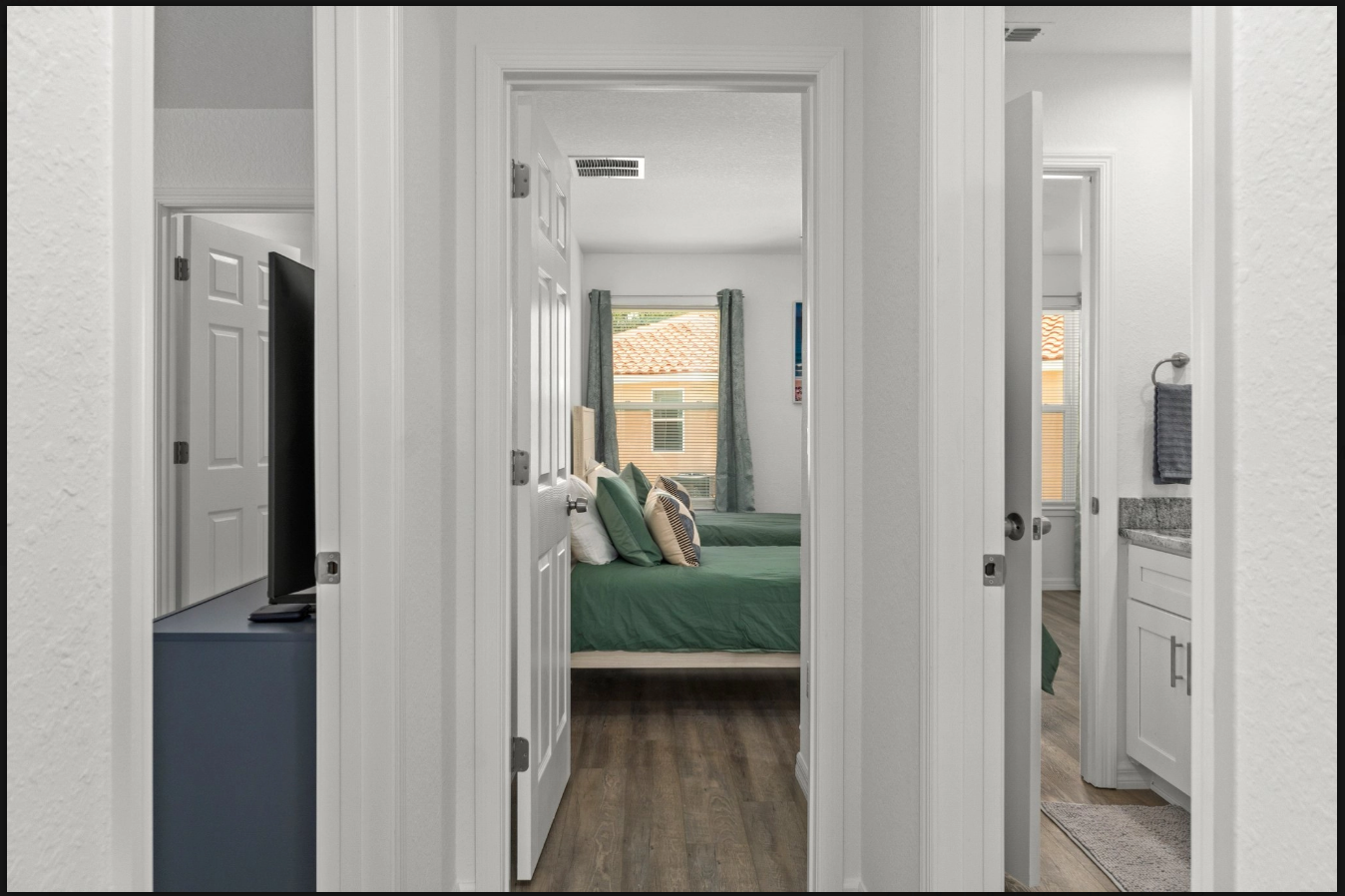 Hallway view into a bedroom with a green bedspread, white doors, and a bathroom visible on the right