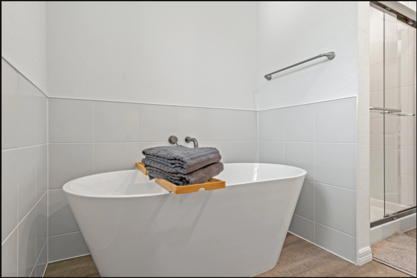 Minimalist bathroom with white soaking tub, folded towels, and glass shower door
