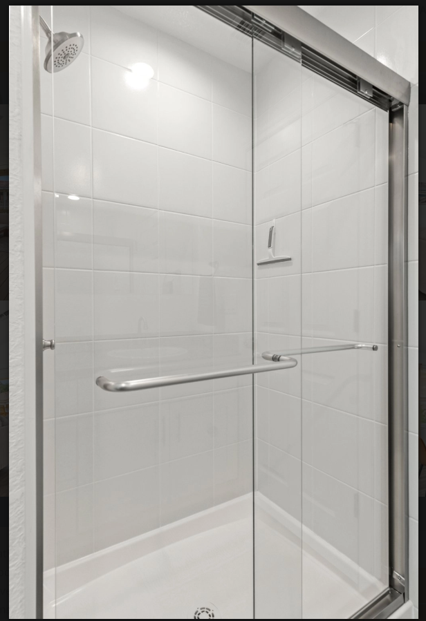 White tiled walk-in shower with glass door and chrome grab bar