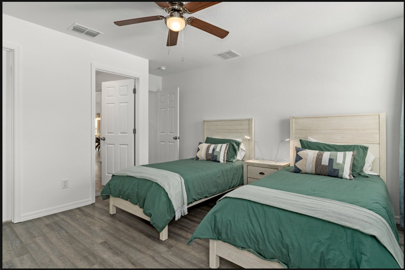 Bright bedroom with two twin beds, green bedding, white walls, and a ceiling fan.