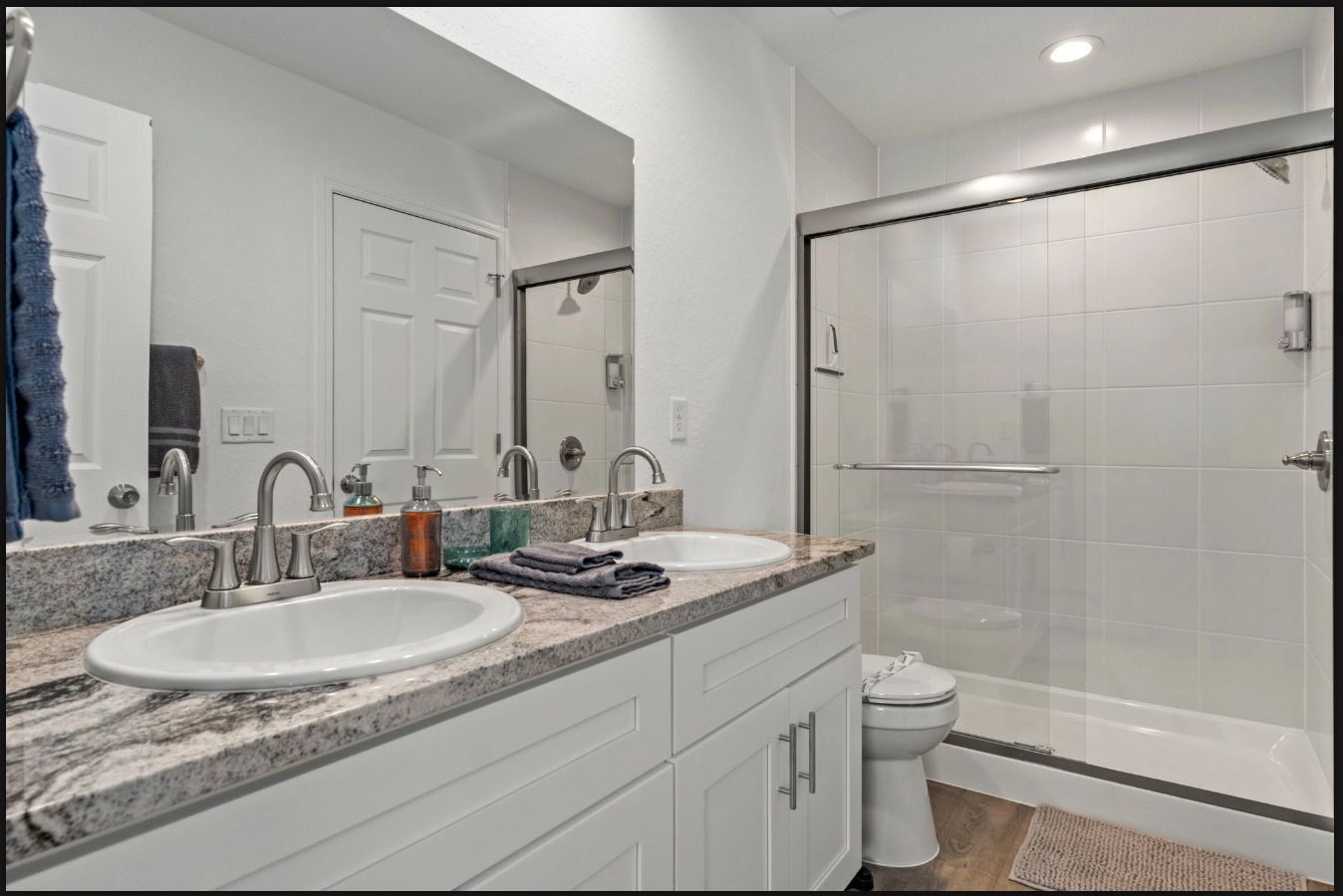 Bright bathroom with double vanity, granite countertop, and glass shower enclosure