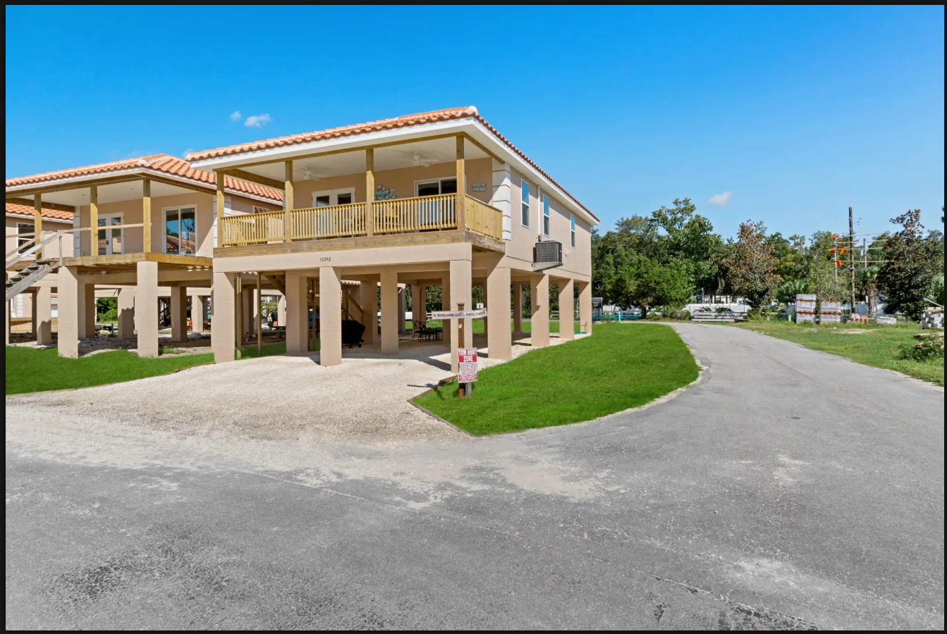 Two-story beige building with a covered entrance beside a paved driveway under a clear blue sky
