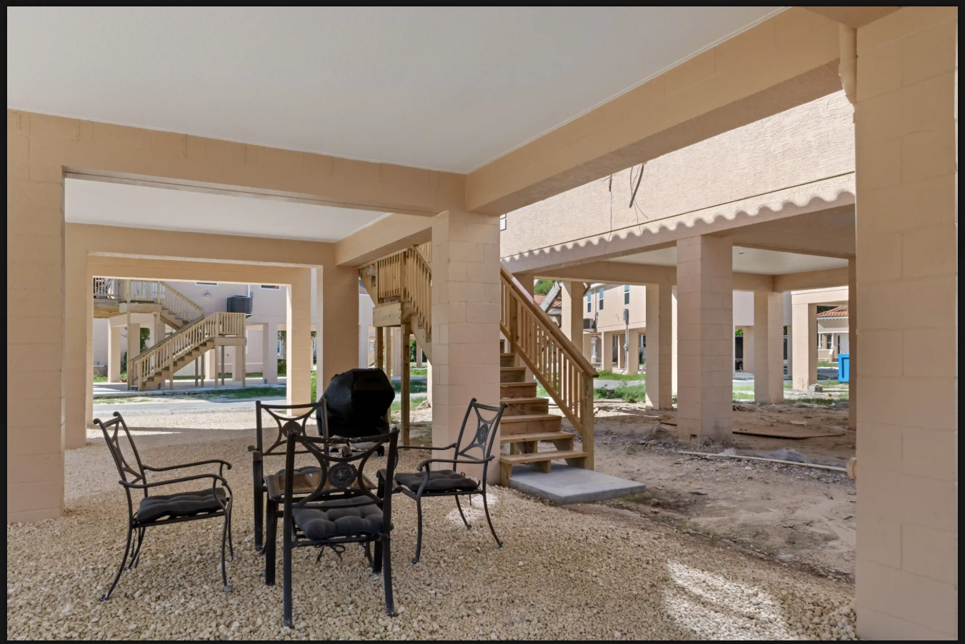 Covered outdoor patio with chairs, table, and stairs beside a pool area under construction