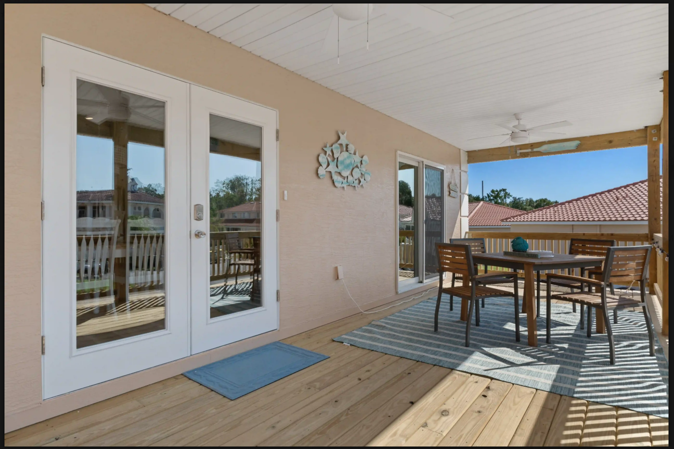 Covered patio with white French doors, wooden dining set, blue doormat, and mountain view