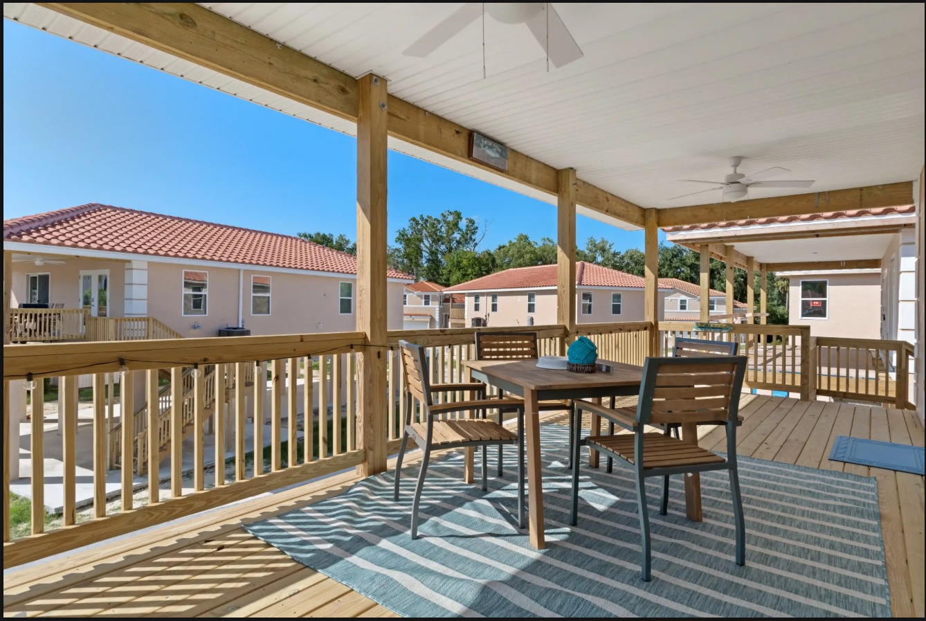 Covered balcony with wicker table and chairs overlooking apartment buildings and blue sky