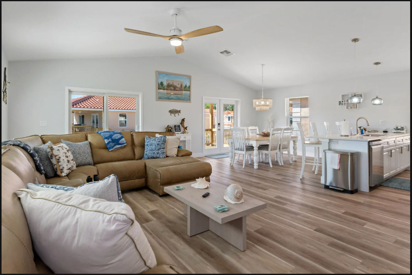 Open-plan living room and dining area with tan sectional, white furniture, and kitchen island in the background