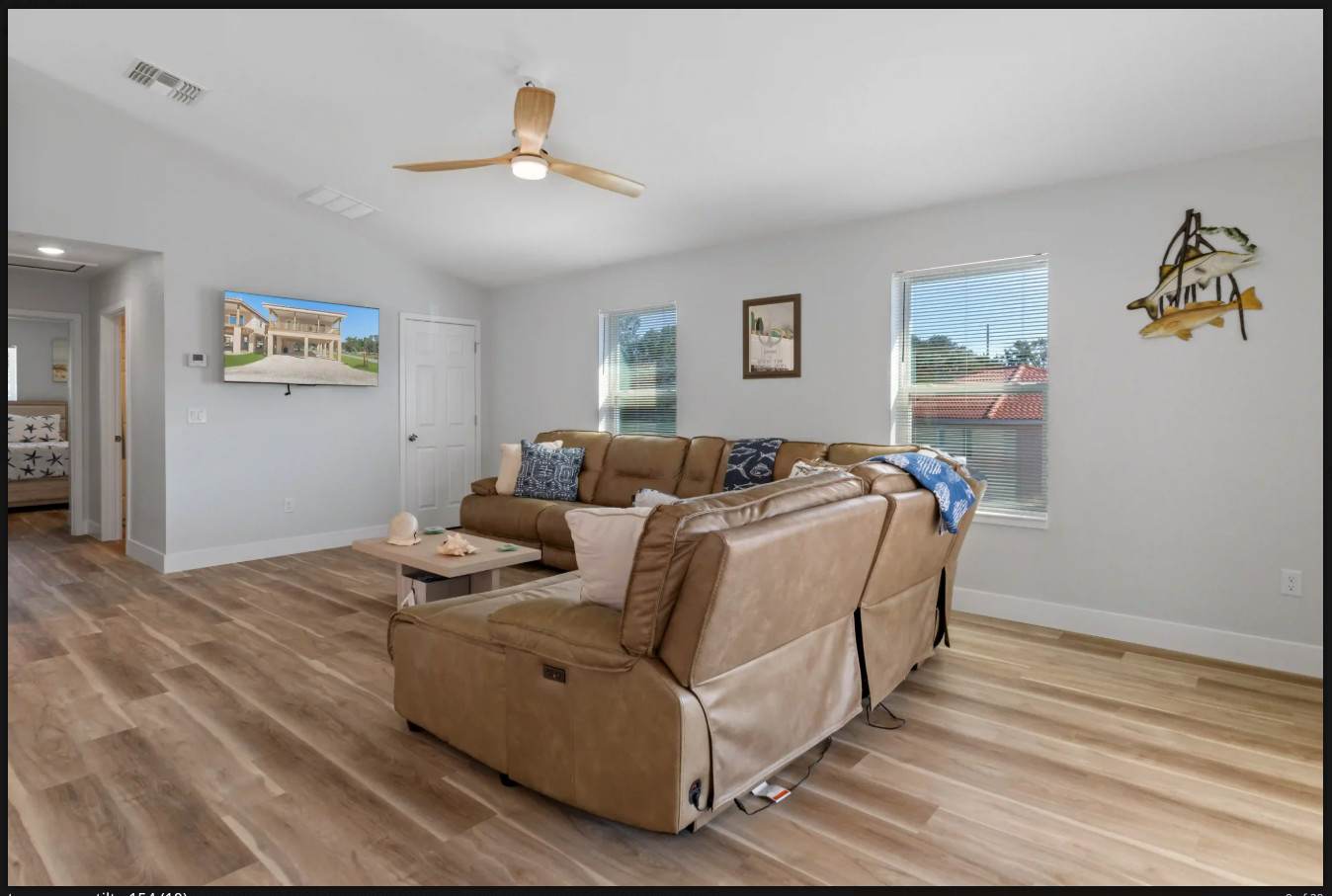 Spacious living room with tan sectional sofa, wood floors, ceiling fan, and wall art on light gray walls