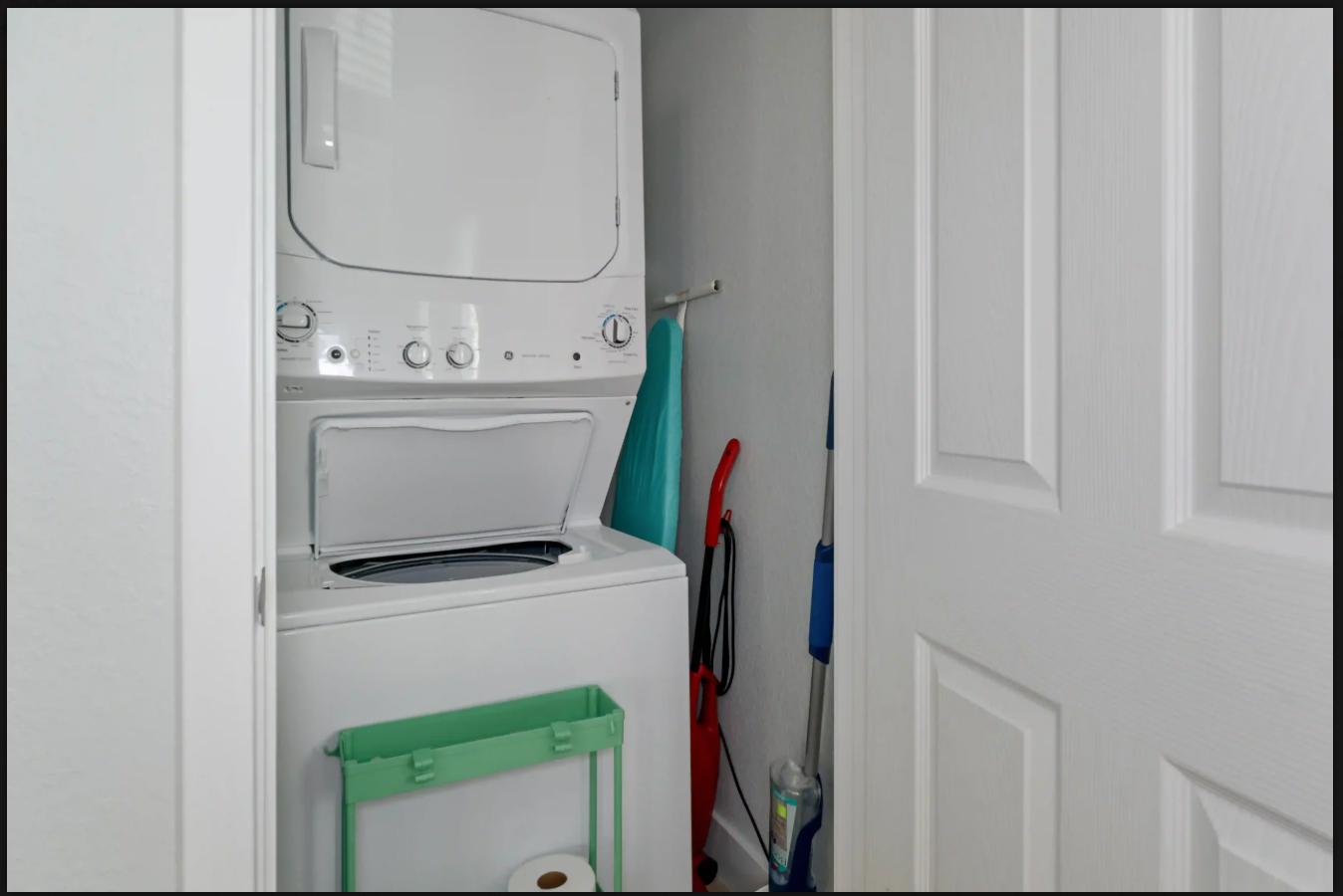 Stacked washer and dryer in a closet, with cleaning tools beside it.