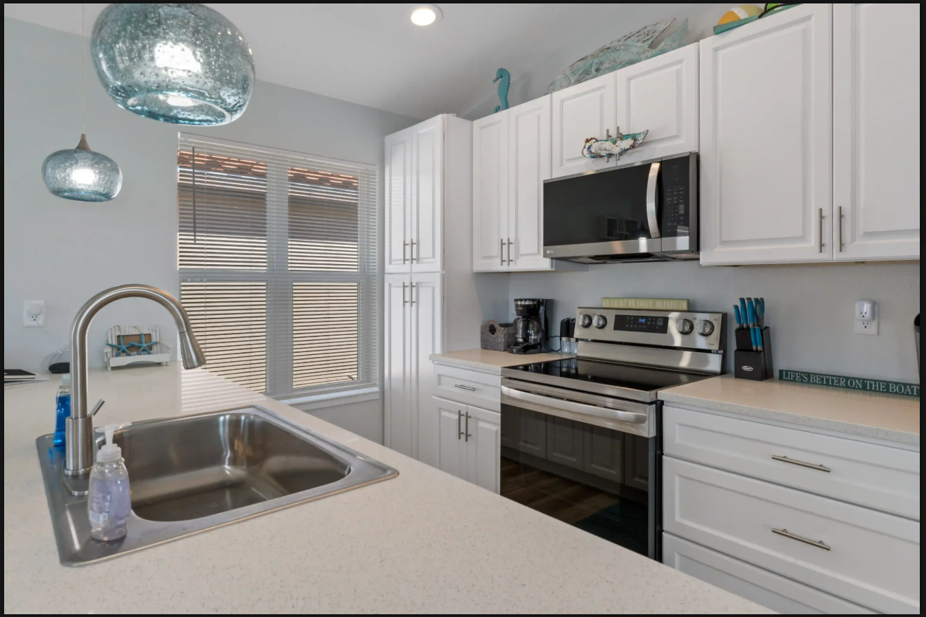 Modern white kitchen with stainless steel appliances, island sink, and blue pendant lights