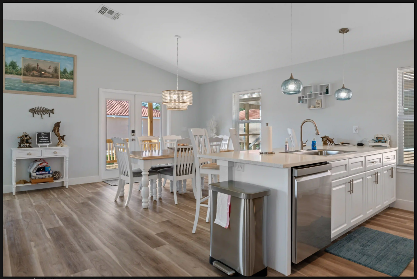 Bright open kitchen and dining area with white cabinets, wood floors, and stainless steel appliances