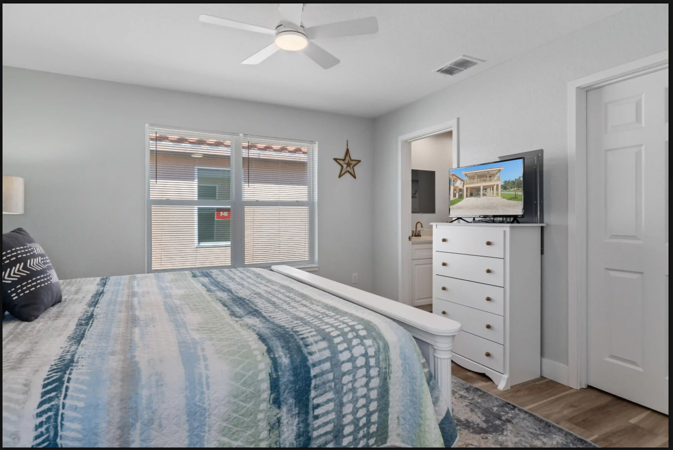 Bright bedroom with a bed, dresser, TV, window blinds, and ceiling fan
