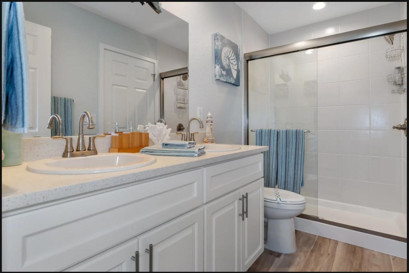 Bright bathroom with white vanity, sink, mirror, and glass shower door with blue towel