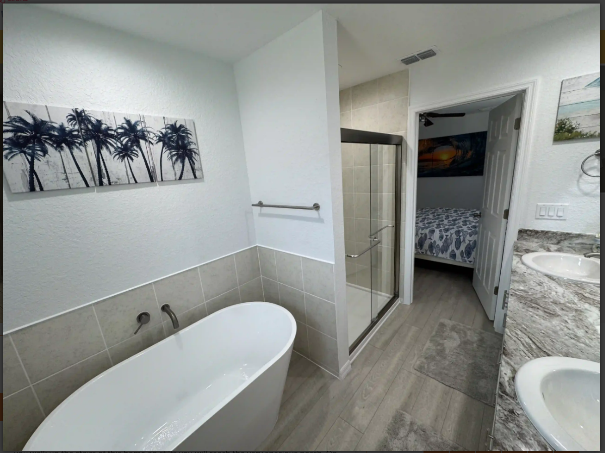 Modern bathroom with a white bathtub, glass shower, and hallway view to a bedroom.