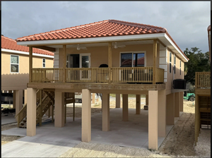 Elevated beige house with red tile roof and wraparound porch on stilts