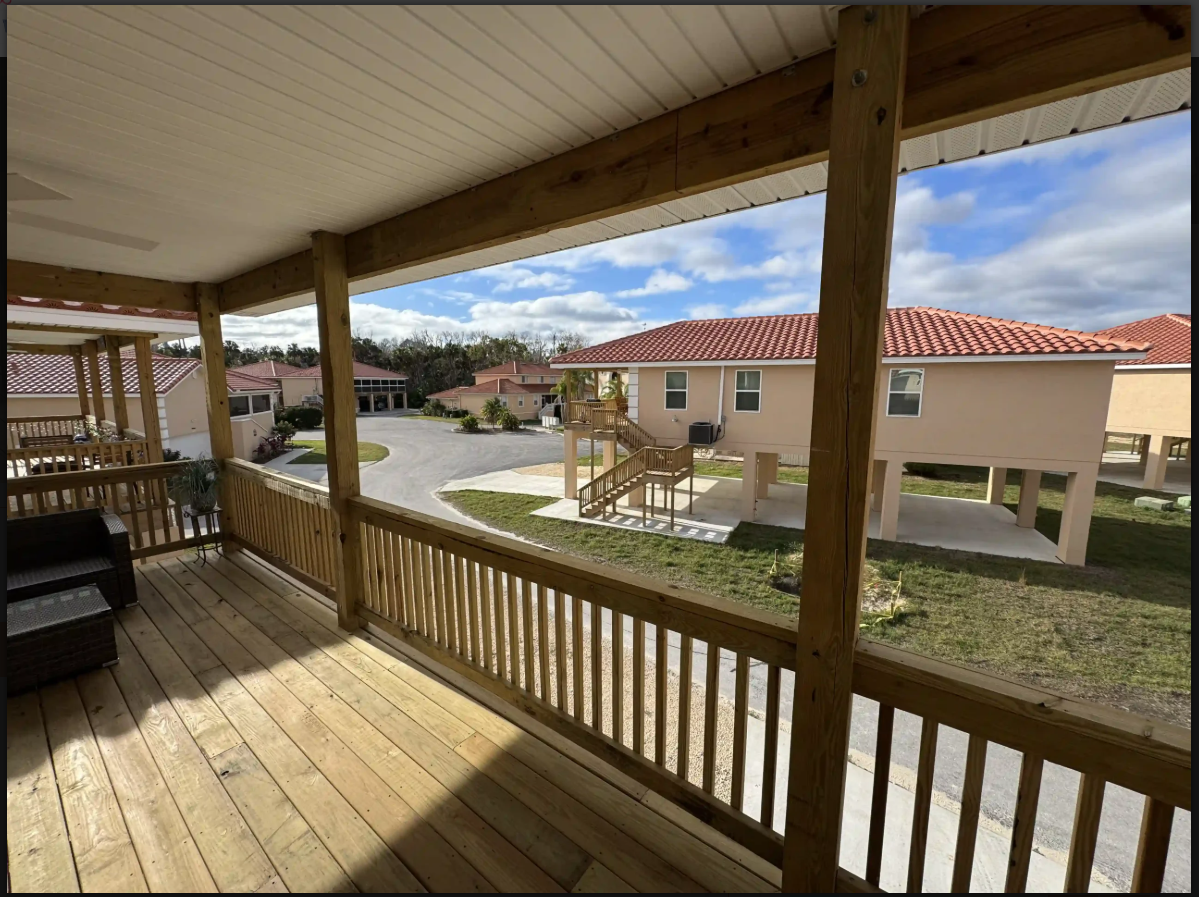 Covered wooden porch overlooking a sunny courtyard with beige houses and red tile roofs