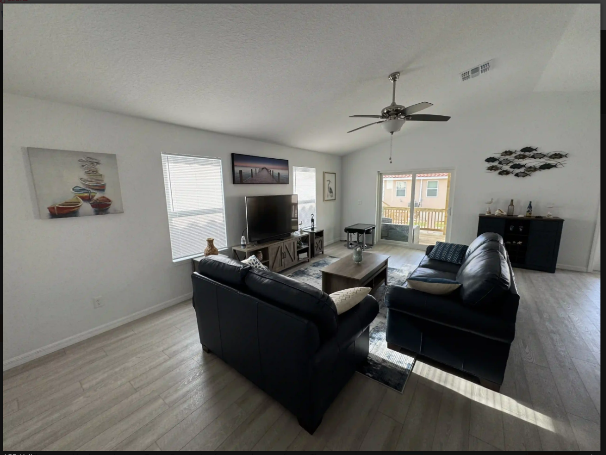 Bright living room with black sofas, TV, ceiling fan, and sliding doors to a patio.