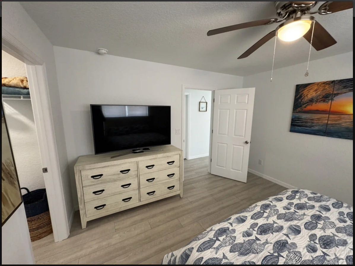 Bedroom with TV on dresser, bed, ceiling fan, and sunset wall art
