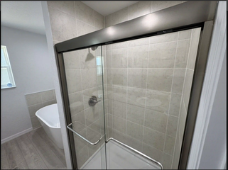 Bathroom with glass shower enclosure beside a bathtub and gray tiled walls
