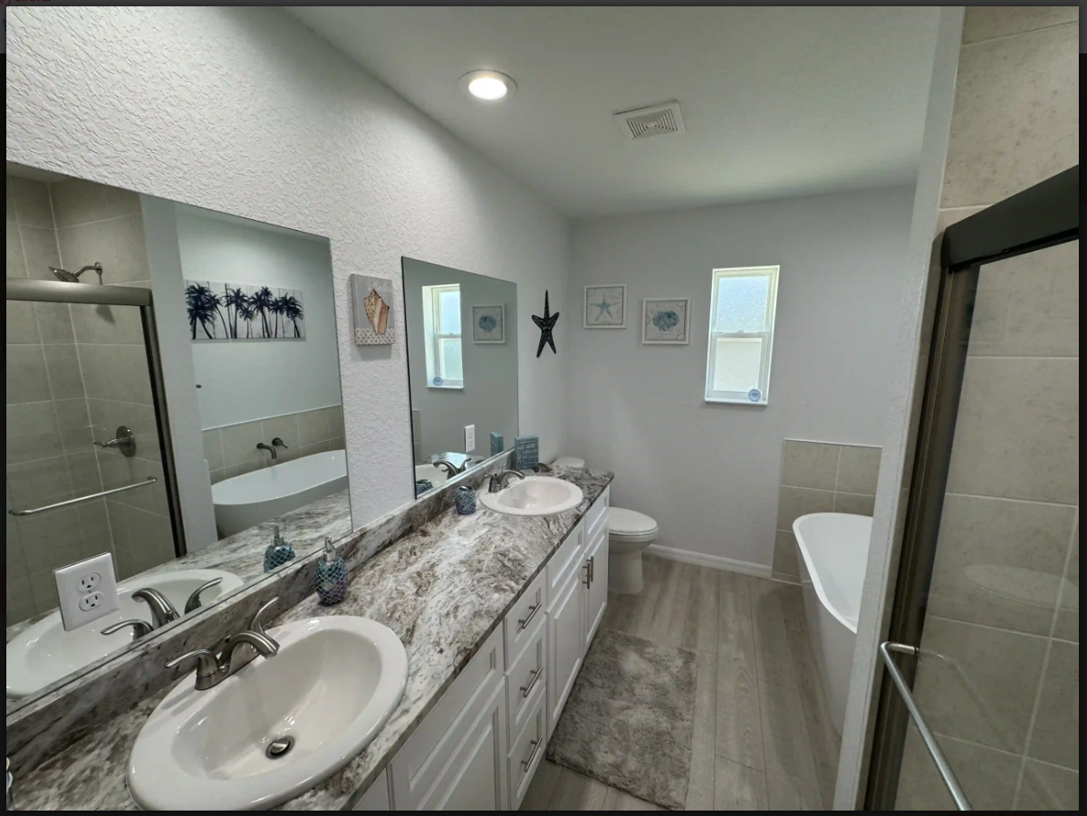 Bright modern bathroom with double vanity, large mirror, bathtub, and walk-in shower through a glass door.