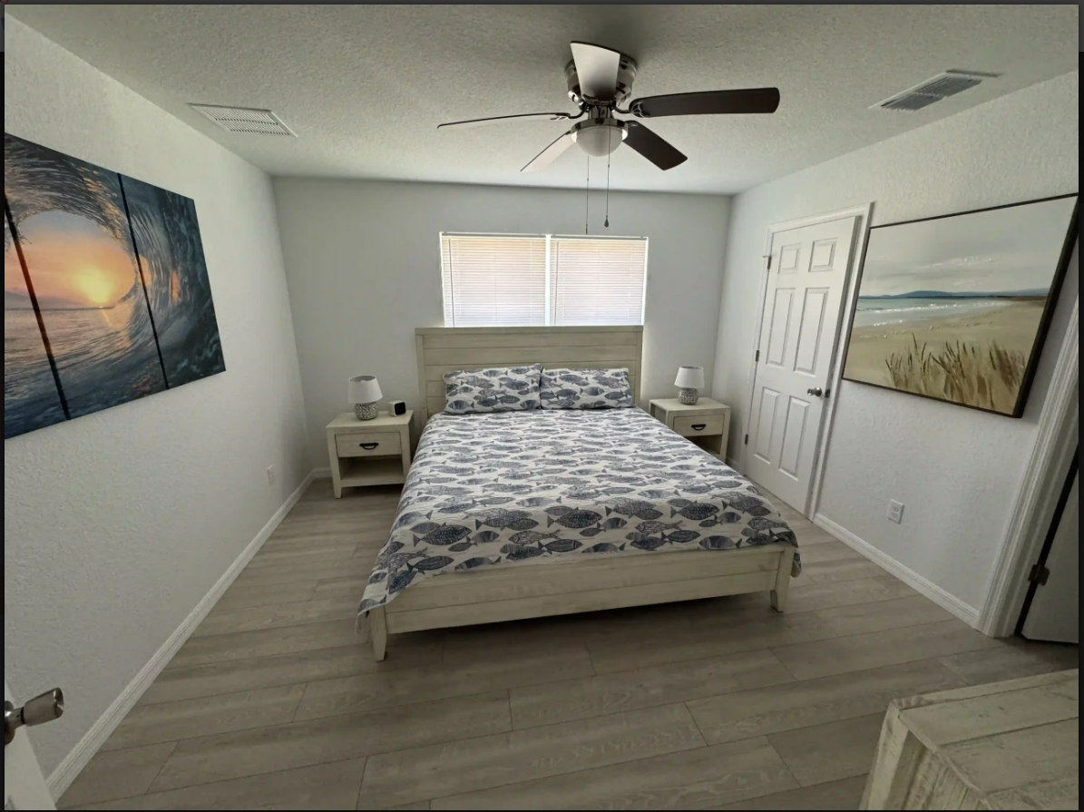 Minimal bedroom with a bed, ceiling fan, white walls, and wall art.
