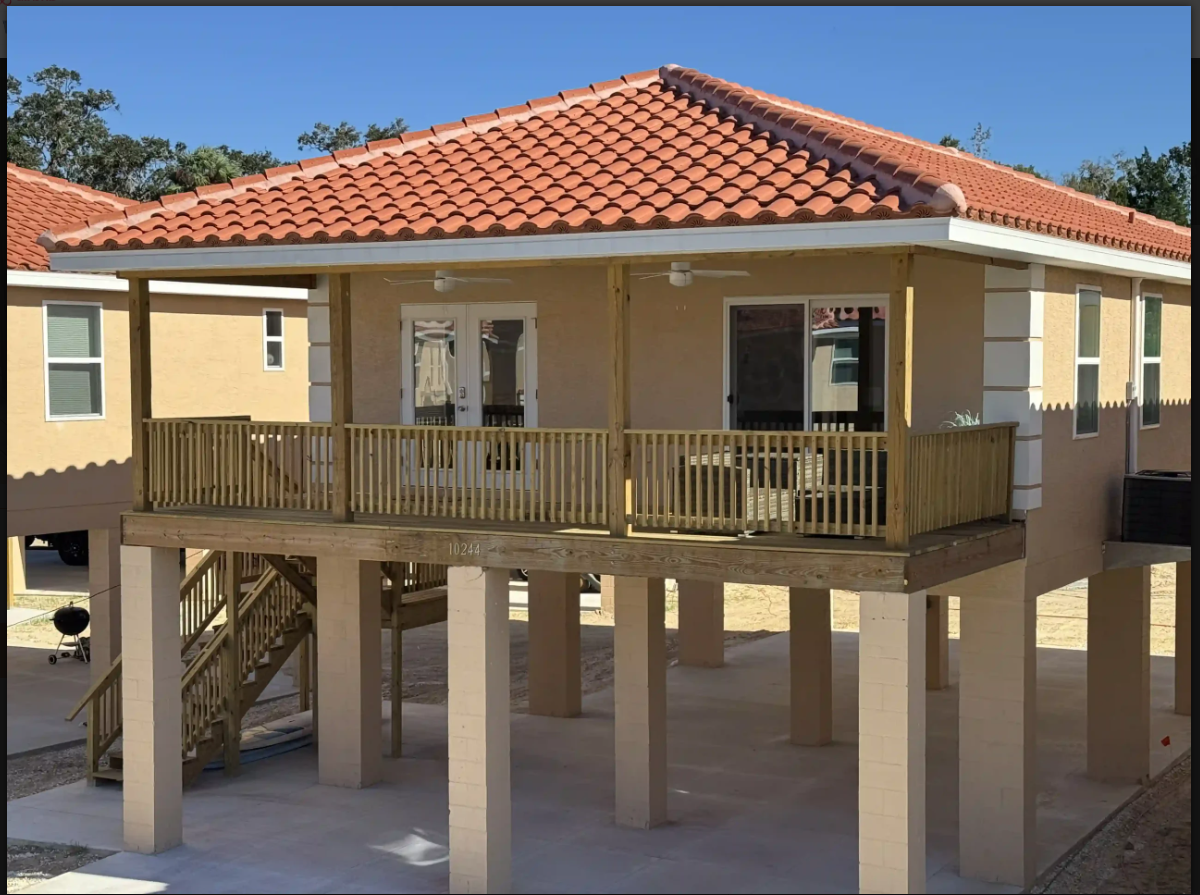 Elevated house with terracotta roof, wooden wraparound porch, and support pillars under the structure