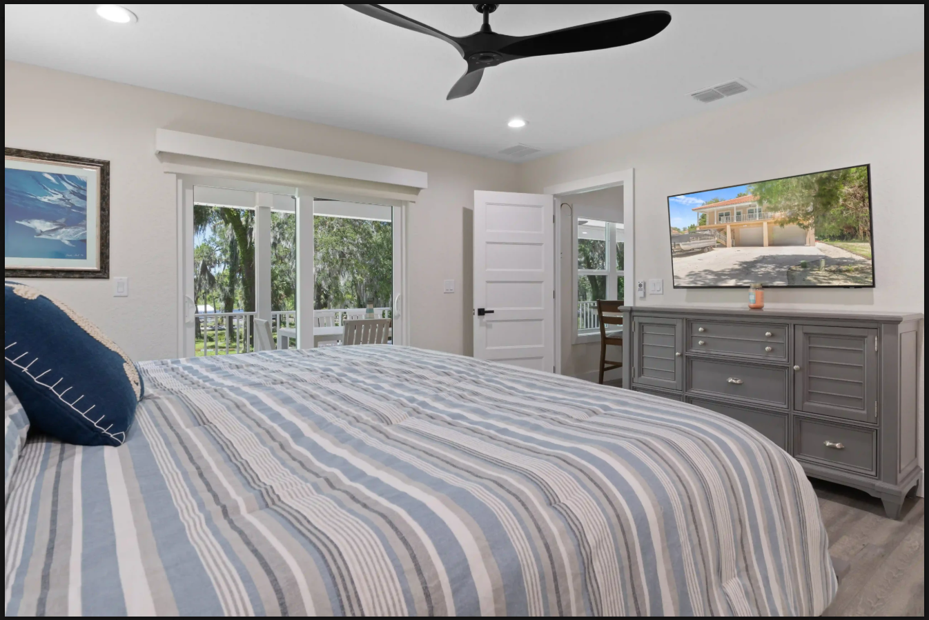 Bright bedroom with striped bedspread, ceiling fan, dresser, and sliding glass doors to a balcony.