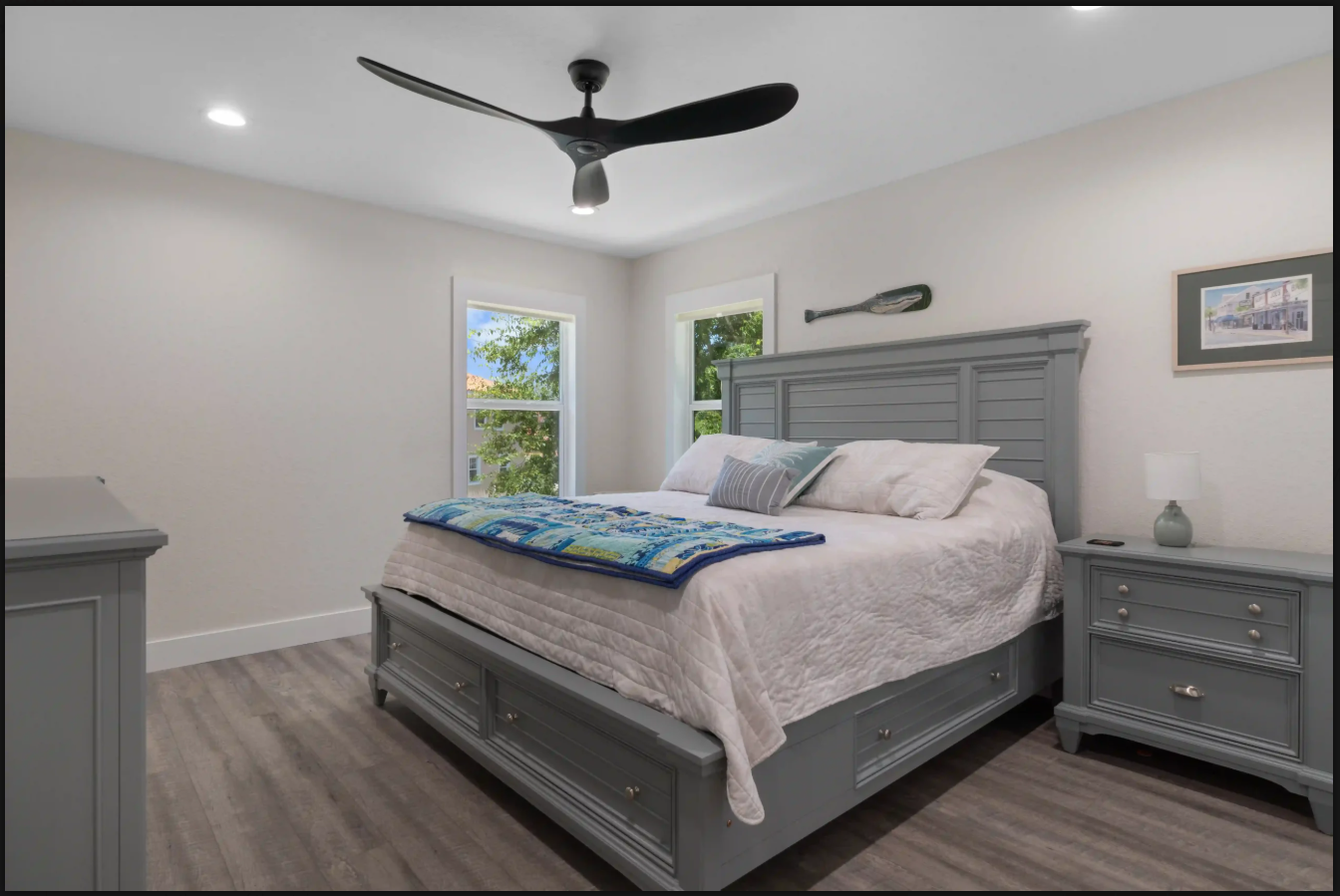 Gray bedroom with a large bed, matching nightstands, windows, and a ceiling fan