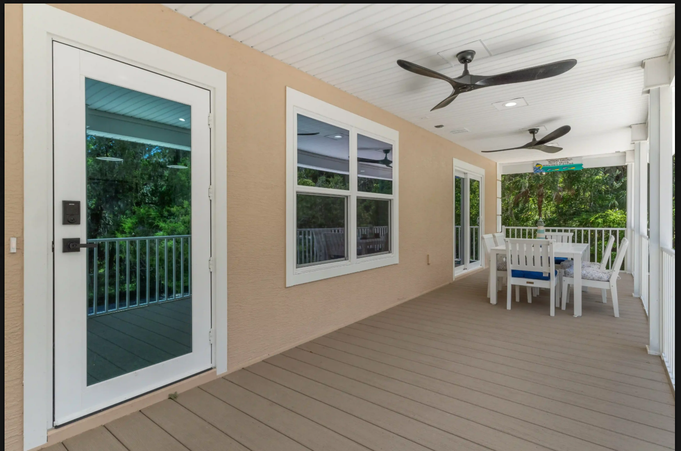 Covered patio with tan flooring, white columns, ceiling fans, and outdoor dining table by glass doors