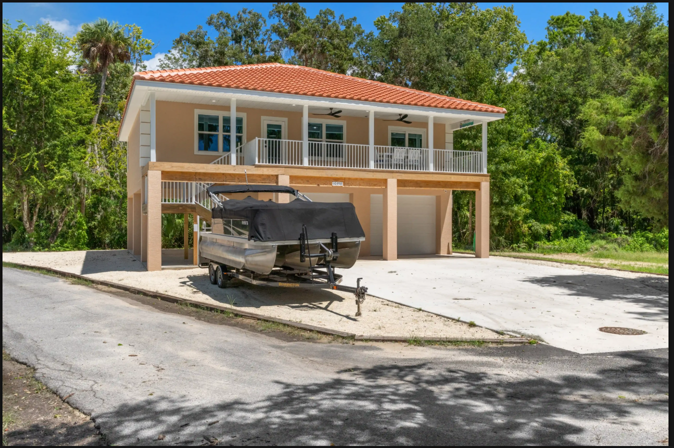 Two-story house with a red tile roof and boat parked in the driveway, surrounded by trees