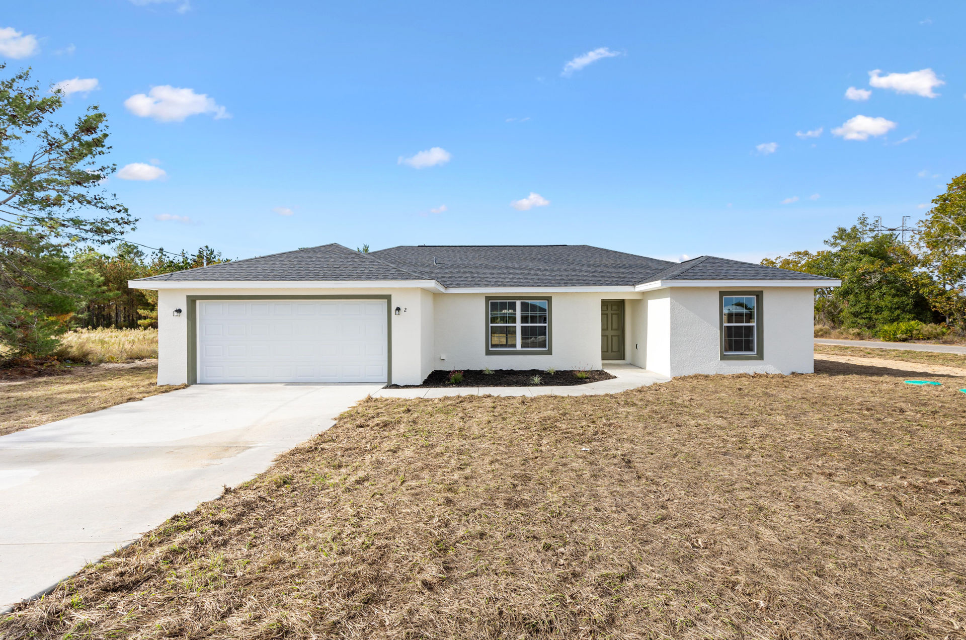 Single-story white house with a two-car garage, concrete driveway, and a dry front yard under a blue sky