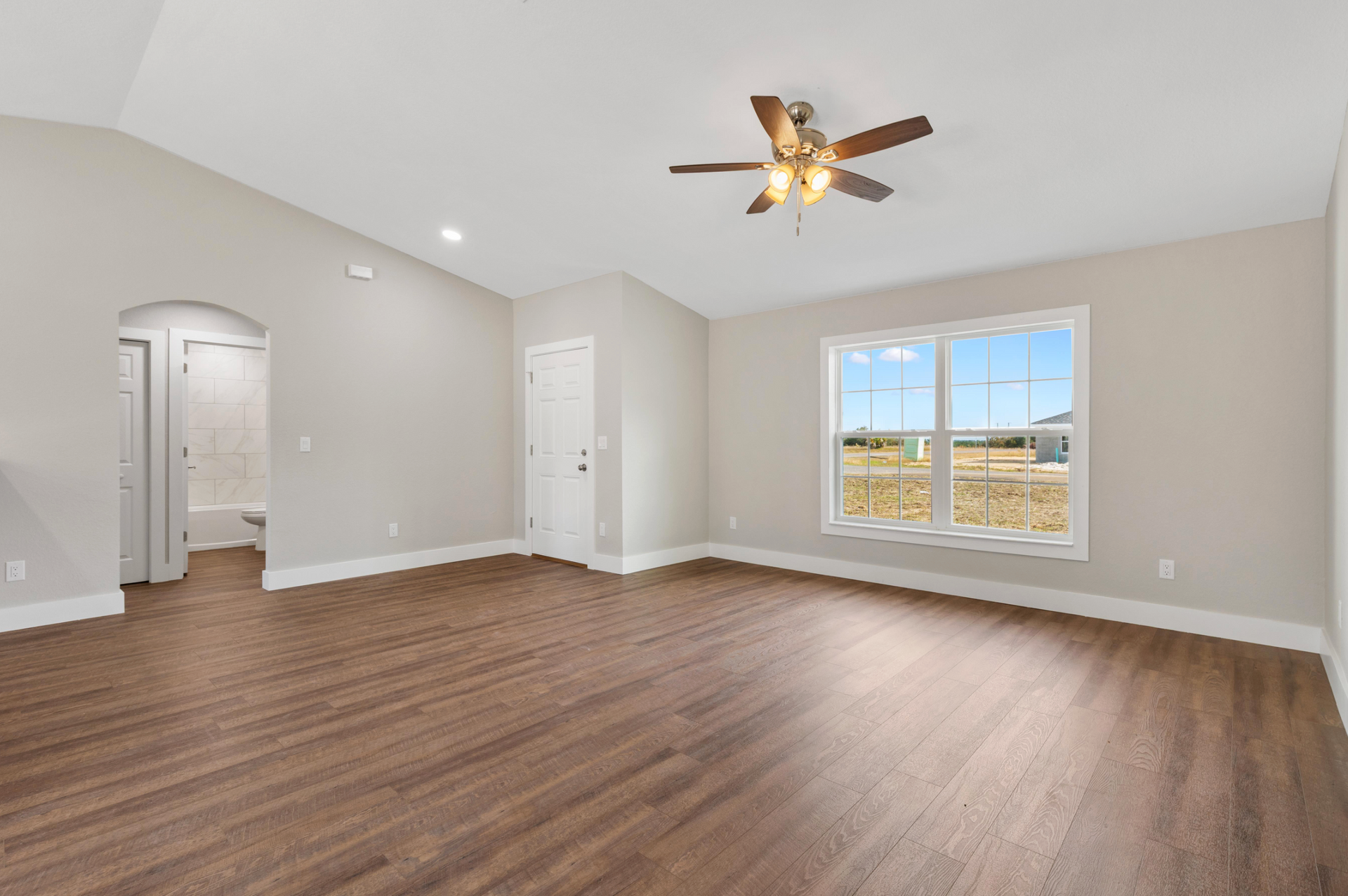 Empty beige living room with wood floors, ceiling fan, and large window with countryside view
