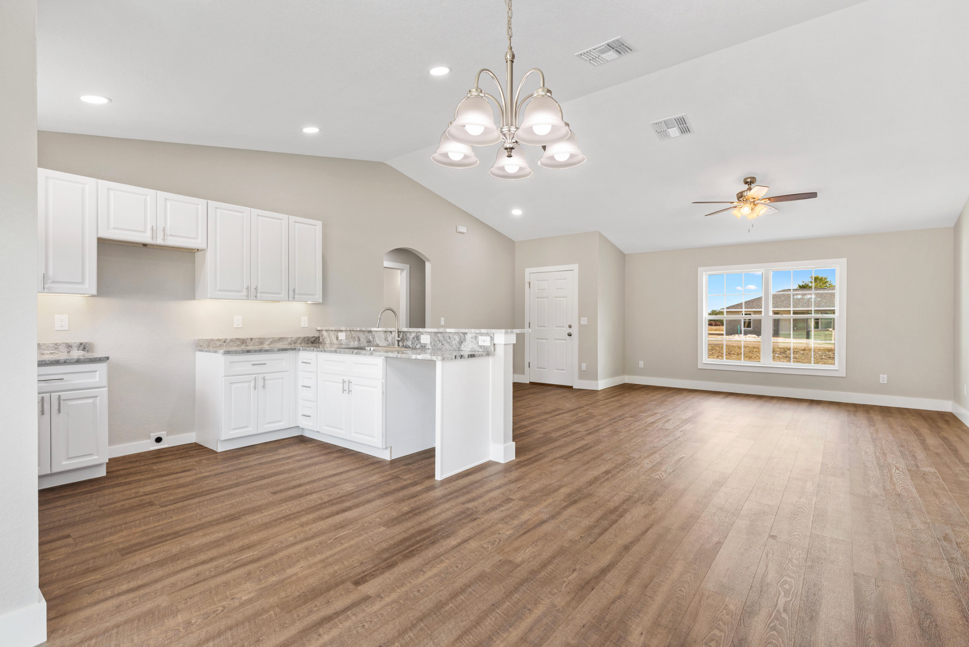 Bright open kitchen and living room with white cabinets, wood floors, and large windows