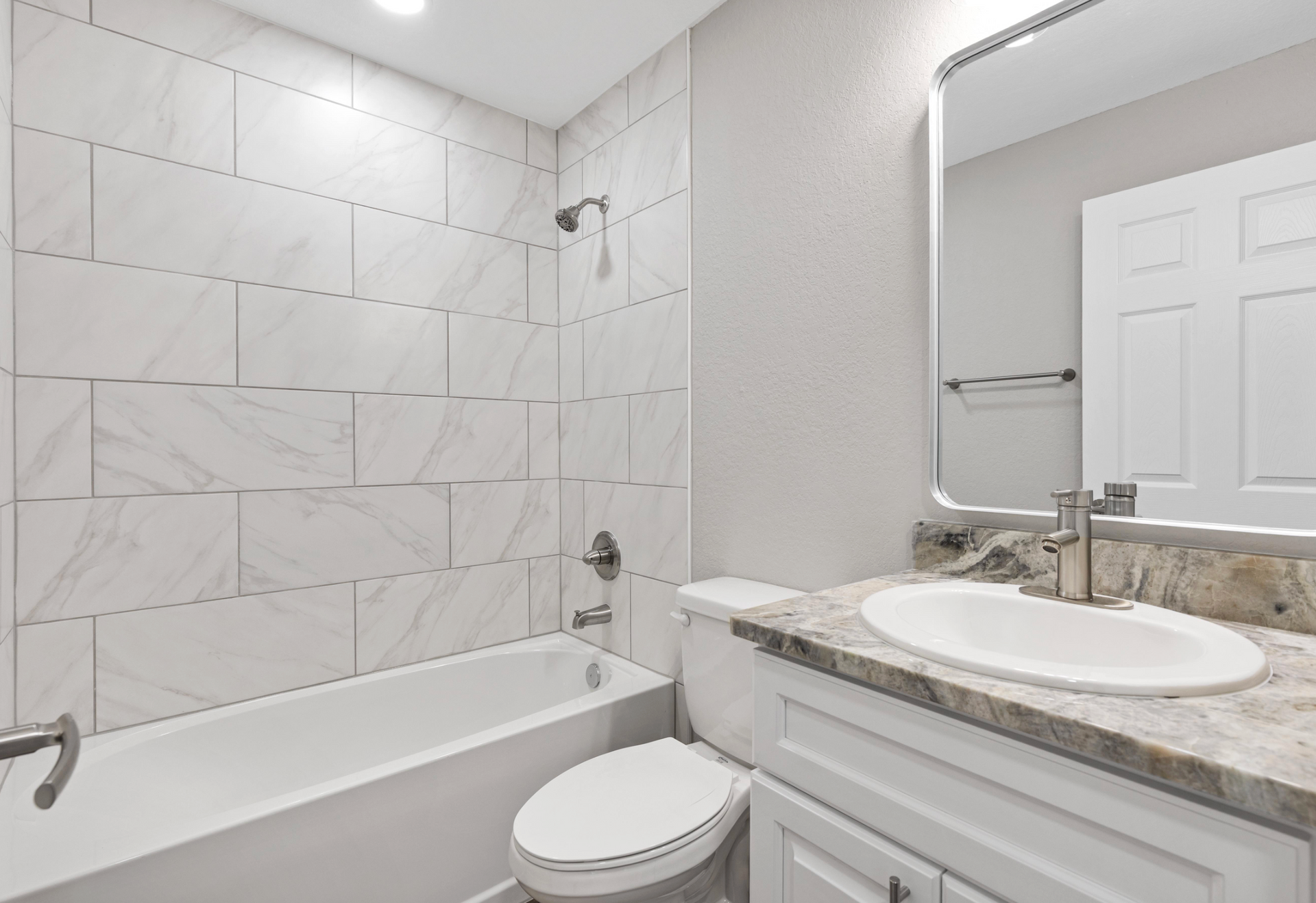 Modern white bathroom with tub, toilet, vanity sink, and large mirror￼